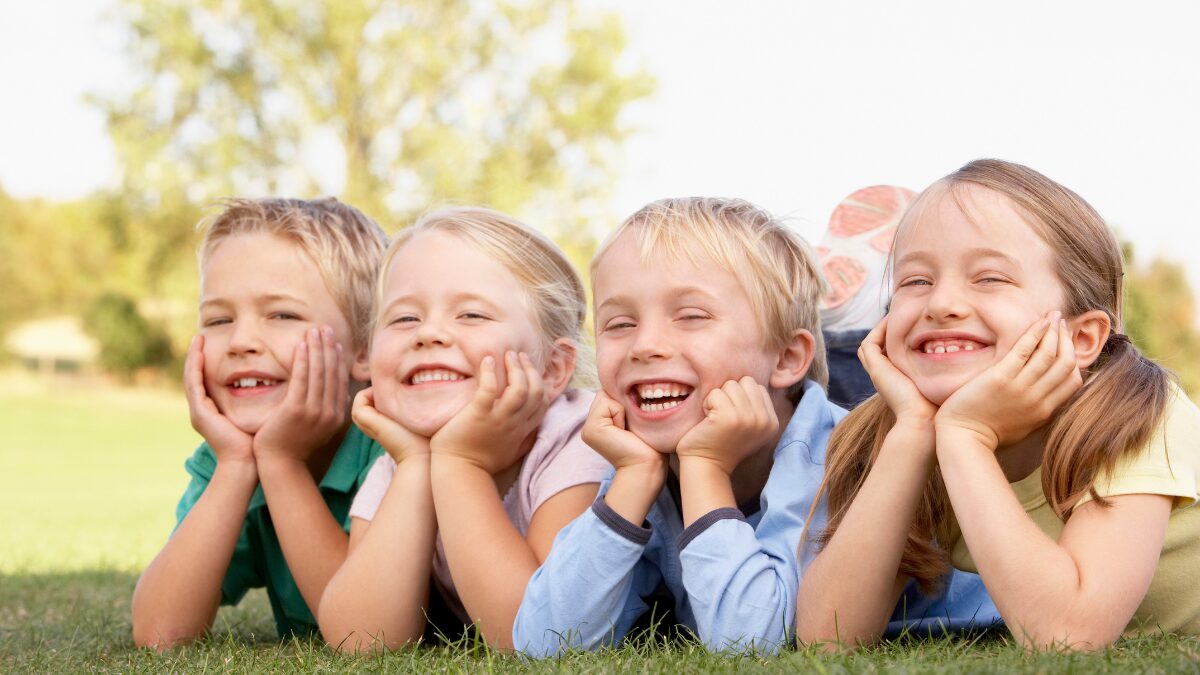 5-6歳の子供達が芝生に寝そべって肘をつきこちらを笑顔で見ている様子